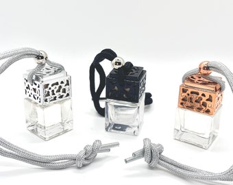 May include: Three car air fresheners with silver, black, and rose gold metal accents. Each air freshener is a small square bottle with a decorative metal cage and a silver string for hanging.