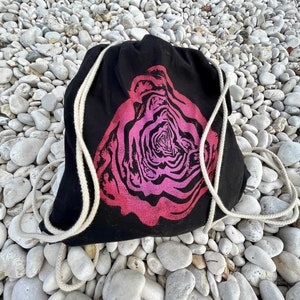 以下が含まれることがあります： ピンクと白のバラのデザインが施された黒い巾着袋。袋には白い紐が付いています。