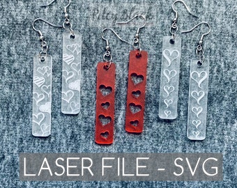 May include: Four pairs of laser cut earrings, two pairs are clear with white hearts and two pairs are red with red hearts. The earrings are displayed on a gray textured surface. LASER FILE - SVG