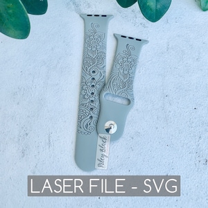 May include: Two gray silicone watch bands with a floral design. The bands are for Apple Watches and are laser cut. The bands are on a white surface with green leaves in the background.