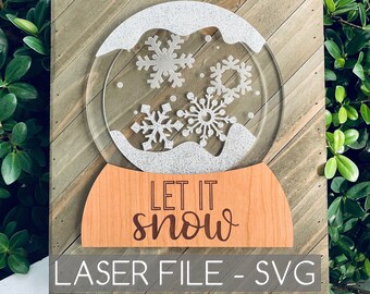 Puede incluir: Un letrero de madera con un globo de nieve blanco con purpurina y las palabras "Let it snow" en letras marrones. El letrero también dice "Laser File - SVG" en letras blancas.