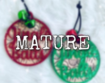 May include: Two round ornaments with red and green fabric and white embroidery. The ornaments have the text "Jingle Balls" on them. The word "MATURE" is written in white letters across the ornaments.