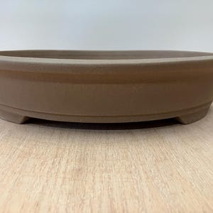 May include: A brown oval ceramic bonsai pot with a raised rim and three small feet on the bottom.