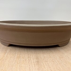 May include: A brown oval ceramic bonsai pot with a slightly raised rim and three small feet on the bottom.