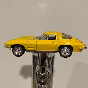 May include: A yellow toy car model of a classic Corvette, mounted on a chrome beer tap.