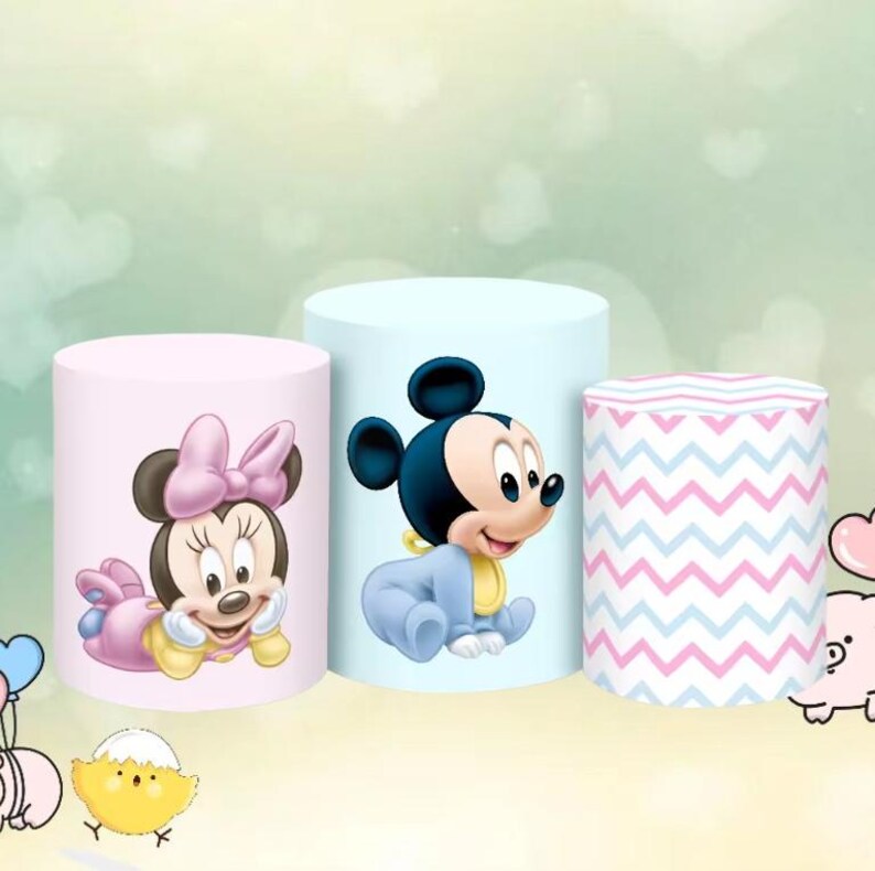May include: Three cylindrical decorations. One is pink with Minnie Mouse, another is light blue with Mickey Mouse, and the third has a pink and blue chevron pattern. The decorations are for a baby shower or birthday.