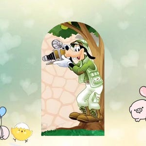 以下が含まれることがあります： 緑色のサファリ衣装を着た、ヴィンテージカメラを持ったグーフィーの漫画の画像。彼は木と石壁の前に立っています。背景はハートの形をした薄緑色です。黄色いひよこと豚が左下と右下の隅にいます。