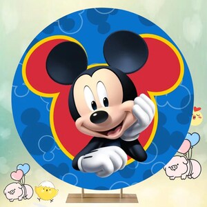 May include: A round blue and red backdrop featuring a cartoon image of Mickey Mouse. Mickey Mouse is smiling and has his hand on his chin. The backdrop is ideal for a birthday party or other celebration.