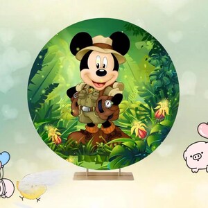 May include: A circular backdrop featuring Mickey Mouse in safari attire, set against a lush green jungle background. Mickey is wearing a khaki outfit, a hat, and a backpack. The backdrop is supported by a wooden stand, with cartoon flowers and foliage.