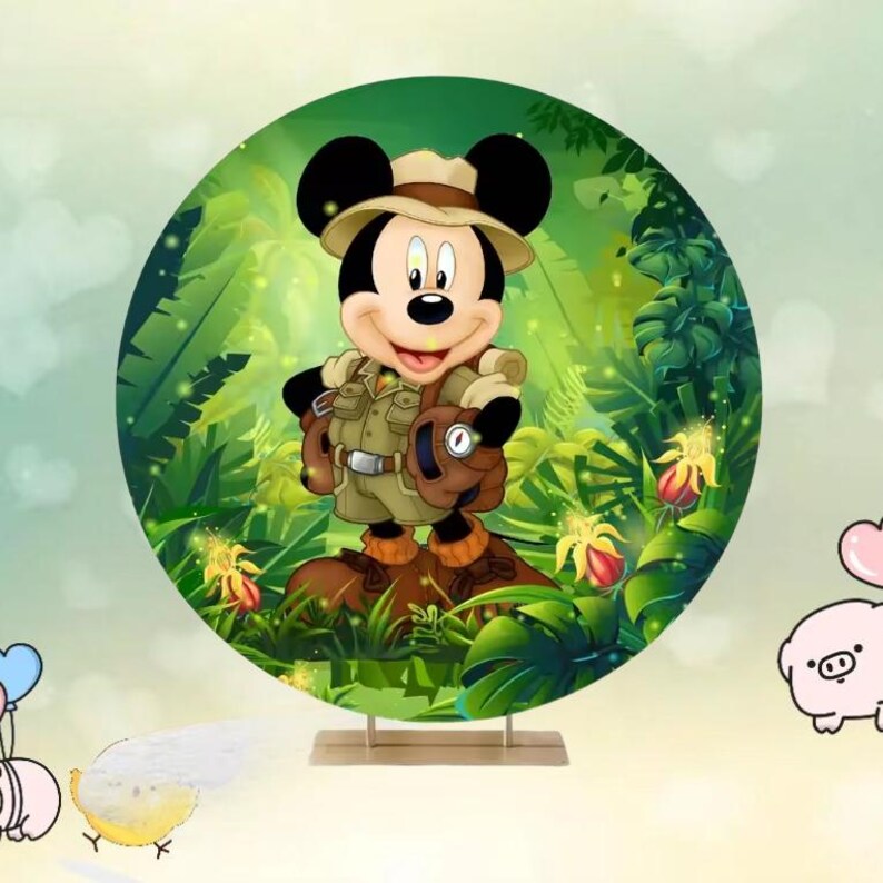 May include: A circular backdrop featuring Mickey Mouse in safari attire, set against a lush green jungle background. Mickey is wearing a khaki outfit, a hat, and a backpack. The backdrop is supported by a wooden stand, with cartoon flowers and foliage.