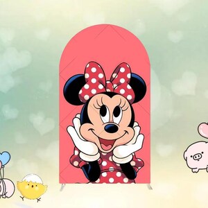 May include: A decorative arch featuring a cartoon image of Minnie Mouse. Minnie Mouse is wearing a red dress with white polka dots and a matching bow. The background is a light pink color.