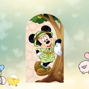 以下が含まれることがあります： 緑色の帽子、ジャケット、ブーツを含む、サファリ衣装を着たミッキーマウスの漫画画像。彼は木のそばに立っており、薄緑色の背景と背景にいくつかの漫画のキャラクターがいます。
