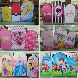 May include: A collection of colorful, arched backdrop stands featuring various designs. Designs include cartoon characters like Pikachu, Disney princesses, and Barbie, as well as polka dots and floral patterns. The stands are likely for parties or events.