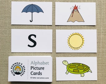 Puede incluir: Un conjunto de tarjetas de imágenes del alfabeto con un paraguas azul, un volcán, un sol, una tortuga y la letra S. Las tarjetas son blancas con contornos negros y forman parte de un conjunto llamado "Miss Rhonda's Readers Alphabet Picture Cards".