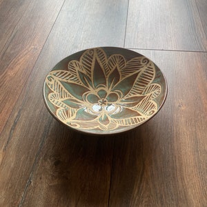 May include: A brown ceramic bowl with a teal glaze and a decorative floral design in a lighter brown colour.