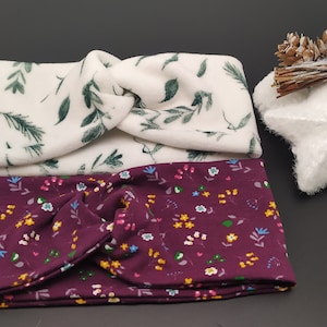 Pode incluir: Duas faixas de cabelo de tecido com um design de nó. A faixa superior é branca com um padrão de folhas verdes. A faixa inferior é bordô com um pequeno padrão floral.