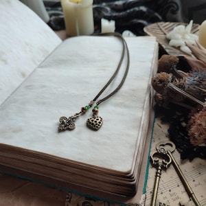 Pu&ograve; includere: Un segnalibro in pelle marrone con un cuore e un ciondolo decorativo a forma di chiave. Il segnalibro &egrave; su un libro con una pagina bianca.