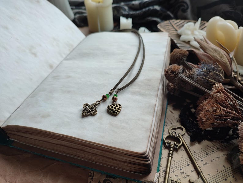 Pu&ograve; includere: Un segnalibro in pelle marrone con un cuore e un ciondolo decorativo a forma di chiave. Il segnalibro &egrave; su un libro con una pagina bianca.