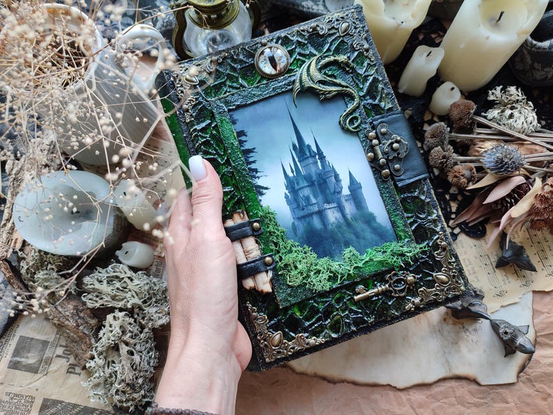 May include: A handcrafted, fantasy-themed journal with a castle illustration. The cover is dark green with ornate metal accents, a dragon embellishment, and a clasp. The journal's design evokes a mystical and gothic aesthetic.