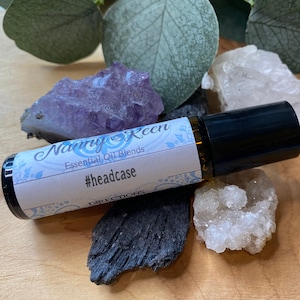 Könnte beinhalten: Eine kleine, durchsichtige Glas-Rollflasche mit schwarzem Verschluss und einem weißen Etikett. Das Etikett trägt die Aufschrift "Nancy Keen Essential Oil Blends" und "#headcase".