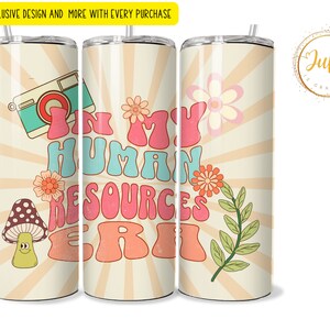 Op de afbeelding: Een witte tumbler met een retro-ontwerp met de tekst "In My Human Resources Era" in kleurrijke, gestileerde letters. De tumbler heeft een bloemenontwerp met een camera en een paddenstoel met een smiley.