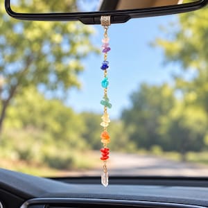 May include: A car rearview mirror hanging ornament featuring a vertical gold-tone chain with seven multi-coloured polished gemstone chips in a rainbow sequence, topped with a decorative metal bead and finished with a clear crystal point pendant.