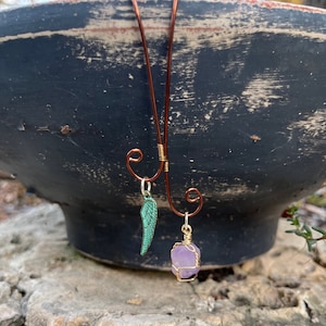 May include: A copper wire necklace with a purple crystal and a green metal wing charm.