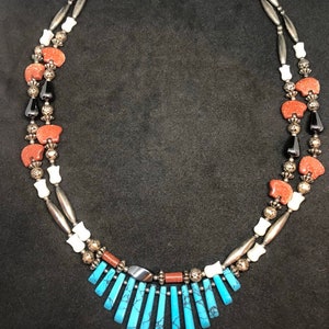May include: A multi-strand necklace with turquoise, red, white, and black beads. The necklace has a pendant made of turquoise stones.
