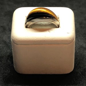 Könnte beinhalten: Ein Ring aus Silber mit einem goldbraunen Tigerauge. Der Ring wird in einer weißen Ringbox präsentiert.