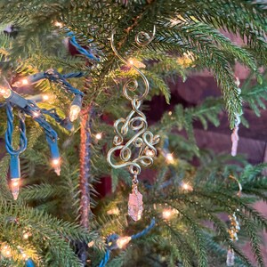 Op de afbeelding: Een gouden draad kerstversiering in de vorm van een boom met een helder kristal dat eronder hangt.