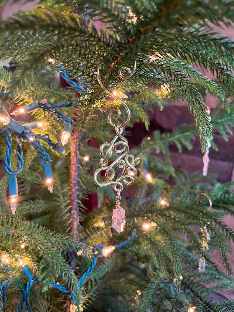 Op de afbeelding: Een gouden draad kerstversiering in de vorm van een boom met een helder kristal dat eronder hangt.