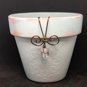 Puede incluir: Una maceta de cerámica azul claro con un diseño de mandala blanco y un cristal colgando de un lazo de alambre.