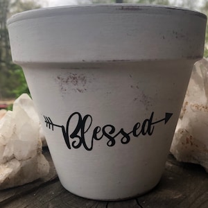 May include: White ceramic planter with a distressed finish and the word "Blessed" written in black with an arrow on either side.