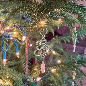 Op de afbeelding: Een gouden draad kerstboom ornament met een roze kristal dat eronder hangt.