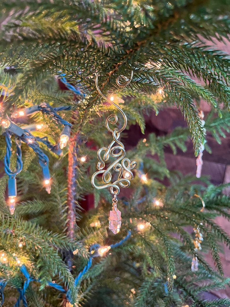 Op de afbeelding: Een gouden draad kerstboom ornament met een roze kristal dat eronder hangt.