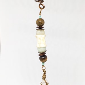 May include: A gold hair coil with a crystal point pendant and beads in shades of brown, white, and turquoise.