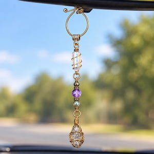 Puede incluir: Un adorno decorativo colgante para el espejo retrovisor del coche con un diseño de alambre dorado. Incluye una cuenta iridiscente transparente, una cuenta morada facetada, una pequeña cuenta metálica y un cristal transparente envuelto.