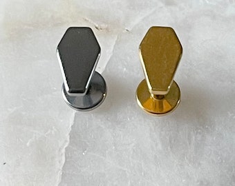 May include: Two coffin-shaped body jewelry pieces, one gold and one black, on a white background.