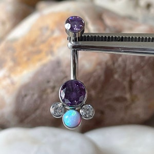 May include: A silver body jewelry piece with a purple gem and a white opal gem. The jewelry is held by a pair of tweezers.