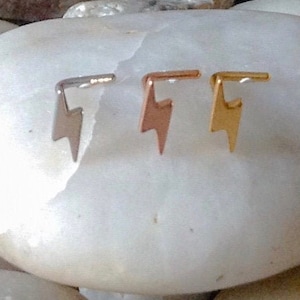 May include: Three nose rings with a lightning bolt design. The rings are silver, gold, and rose gold.