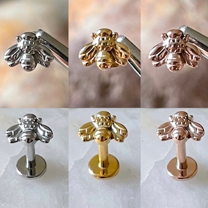 May include: Three bee-shaped body jewellery pieces in different colours. The jewellery is made of surgical steel and comes in silver, gold, and rose gold. Each piece features a detailed bee design with wings and a textured body.