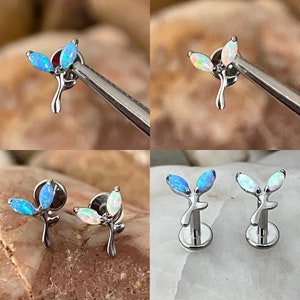 May include: Two pairs of opal flower cartilage earrings. One pair is blue opal and the other is white opal. The earrings are made of surgical steel and have a flat back.