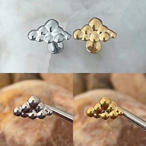 May include: Two silver and gold cloud-shaped body jewelry pieces. The jewelry is made of small, round beads that are clustered together to form a cloud shape. The jewelry is designed to be worn as a cartilage piercing.