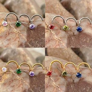 May include: A set of six nose rings with different coloured gemstones. The rings are made of either gold or silver and feature a variety of colours, including red, green, blue, purple, and yellow.