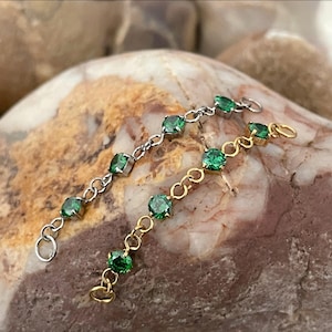 May include: Two delicate jewelry connector chains, one in silver-tone metal and one in gold-tone metal, each featuring four small, round, vibrant green faceted stones set in prongs and linked by circular metal rings at both ends.