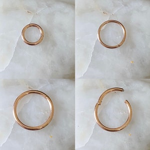 May include: Four gold-coloured seamless hoop earrings in different sizes. The earrings are shown against a white marble background.