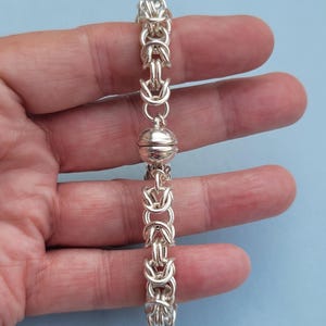 K&ouml;nnte beinhalten: Ein silbernes Armband mit einem magnetischen Verschluss. Das Armband besteht aus einem Kettenglieddesign.