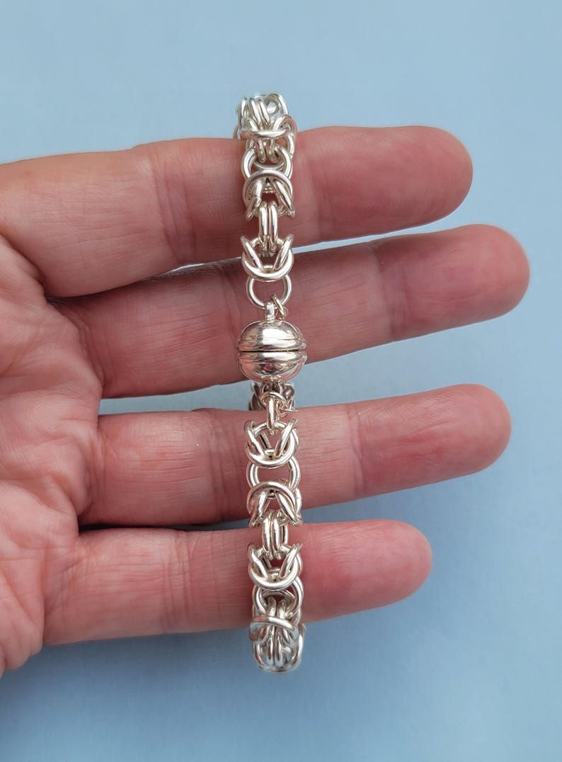 K&ouml;nnte beinhalten: Ein silbernes Armband mit einem magnetischen Verschluss. Das Armband besteht aus einem Kettenglieddesign.