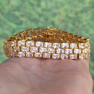 May include: A gold bracelet with a triple row of clear rectangular stones.
