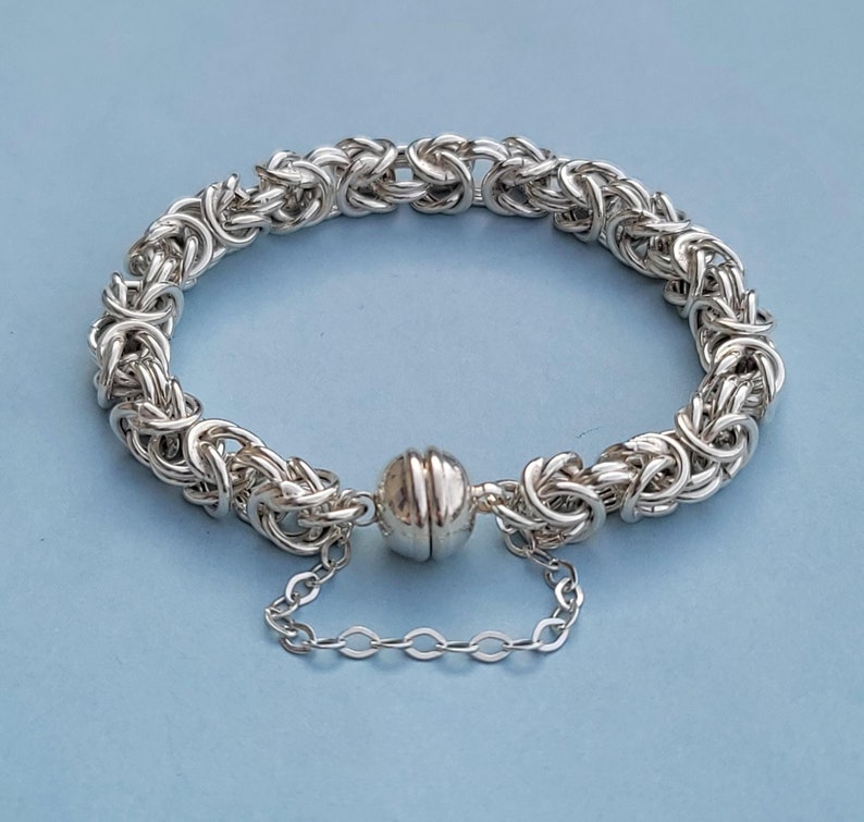 K&ouml;nnte beinhalten: Ein silbernes Kettenarmband mit einem magnetischen Verschluss. Die Kette besteht aus ineinandergreifenden Ringen.